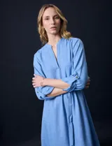 Vestido maxi color beige, con cuello mao y escote en V. Presenta mangas largas con presilla y botón para regular el largo, y un lazo ajustable en la cintura que marca la silueta.