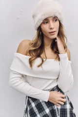 Buzo de punto color blanco, con escote tipo bote que deja los hombros al descubierto y mangas largas ajustadas.