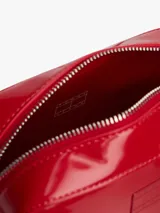 Cartera tipo bandolera de Tommy Jeans con acabado brillante y liso. Presenta un diseño rectangular con cierre de cremallera superior, correa ajustable y una insignia con el logo de la marca grabado en el centro de la parte frontal.