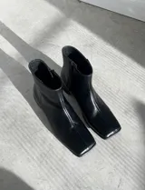 Botas de caña corta de cuero negro, con puntera cuadrada, taco bajo y cierre lateral interno.