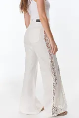 Pantalón de jean negro de pierna ancha con cortes laterales y godets triangulares en tela de broderie o encaje color crudo para mayor amplitud.