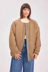 Campera acolchada reversible con capucha, diseño de matelassé, cierre frontal y puños elásticos. Presenta un lado en color verde oliva y otro en color beige.