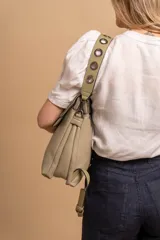 Mochila tipo cartera con tapa, confeccionada en símil cuero color suela. Cuenta con doble compartimento, división interna, cierre de seguridad y bolsillo trasero con cierre. Incluye una correa frontal decorativa con tachas metálicas.