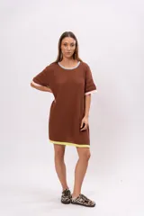Vestido corto marrón de tejido de punto con cuello redondo y mangas cortas. Presenta ribetes en color celeste en el cuello, rosa en las mangas y amarillo en el ruedo.