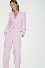 Blazer entallado color lila sin solapa, con escote en V, manga larga y bolsillos con solapa en los laterales. Presenta detalle de encaje combinado a tono en el escote y cierre frontal con un botón forrado.