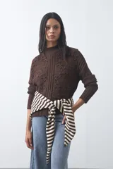 Polera de tejido de punto color marrón, con cuello alto y diseño de textura con relieves y trenzas. Posee mangas largas con puños acanalados.