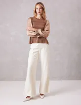 Blusa de punto con torso texturizado en color marrón con hilos de lurex dorados. Presenta un corte peplum con volado en la cintura y mangas largas de satén fluido con volumen, terminadas en puños elásticos fruncidos.