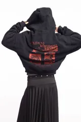 Campera negra de algodón con cierre frontal, capucha, bolsillos laterales y detalles de tachas metálicas en la capucha y los bolsillos. Presenta un estampado frontal con texto en tono rojizo.