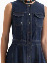 Vestido largo de denim azul oscuro, sin mangas, con cuello mao y cierre frontal de botones. Presenta dos bolsillos con solapa en el pecho y costuras decorativas. La falda es acampanada.