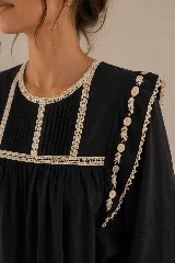 Blusa negra de algodón con cuello redondo, mangas largas y corte holgado. Presenta delicados detalles de puntilla en color natural alrededor del cuello y el canesú, además de bordados florales en los hombros.