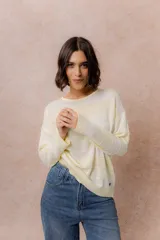 Buzo de tejido liviano con diseño de rayas horizontales en tonos amarillo manteca y blanco, cuello redondo y mangas largas con puños tejidos.