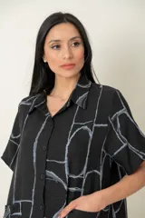 Camisa larga negra con estampado de líneas geométricas en gris, de manga corta y dos bolsillos delanteros.