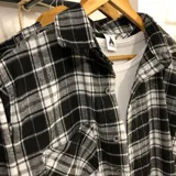 Sobrecamisa de franela a cuadros blancos, negros y grises, de manga larga, con cuello camisero, cierre abotonado y bolsillo en el pecho.