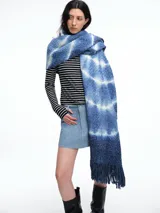 Bufanda de punto grueso tejida en lana, con diseño teñido mediante técnica shibori en tonos azules y blancos, y terminación con flecos en los extremos.