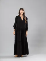 Vestido largo negro con escote en V y detalle de frunces en los hombros. Tiene mangas largas con elástico en los puños y volados en el ruedo.