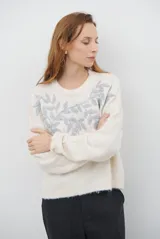 Buzo de tejido de punto en color beige, con cuello redondo y mangas largas. Presenta un delicado bordado de ramas y hojas en color crema en la parte superior del frente.
