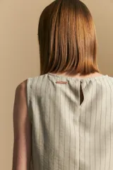 Top sin mangas color beige con finas rayas verticales negras. Presenta un diseño con lazada ajustable en el lateral de la cintura.