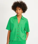 Camisa de manga corta confeccionada en mezcla de viscosa y lino color turquesa. Presenta cuello camisero con escote en V, bolsillos frontales de parche y cierre frontal con botones geométricos de efecto carey.