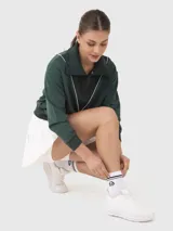 Buzo de medio cierre color verde oscuro con cuello polo y detalle de ribete blanco en forma de V. Presenta puños y cintura acanalados, con mangas largas de diseño holgado.