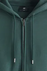 Campera con capucha de felpa de peso medio con interior cepillado suave. Presenta hombros caídos, cierre frontal, bolsillos tipo canguro y cordones ajustables en la capucha. Los puños y el bajo están terminados en punto acanalado.