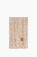 Bufanda tejida en punto trenzado color beige, con detalle de etiqueta de cuero sintético en una esquina.
