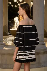 Minivestido negro con rayas horizontales blancas, diseño con hombros descubiertos, mangas voluminosas y volados en el ruedo.