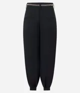 Pantalón de sastrería modelo aladim, color negro, confeccionado en crepé. Presenta pliegues en la cintura, corte holgado con piernas anchas que se estrechan en los tobillos y detalle de cinturón de cadena metálica.