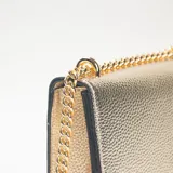 Bandolera de textura granulada en color dorado, con cierre de solapa y correa de cadena metálica dorada con refuerzo de cuero sintético para el hombro.