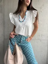 Musculosa blanca de diseño ligero con escote en V y sutiles detalles bordados tonales en el frente, complementada con volados en las sisas.