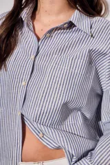 Camisa de corte oversize con diseño de rayas verticales en tonos azul y blanco. Presenta cuello clásico, cierre frontal con botones y mangas largas con puños abotonados.