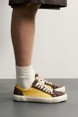 Zapatilla de estilo retro fabricada en una combinación de piel con acabado serraje y algodón, en tonos marrón y amarillo, con suela contrastada.