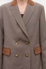 Blazer de corte sastre con estampado de cuadros pequeños en tonos tierra. Presenta solapas y detalles en los bolsillos de gamuza en color marrón, cierre frontal de doble botonadura y estructura entallada.