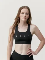 Top deportivo negro de alta sujeción con tecnología performance y motivo estampado reflectante en la espalda.