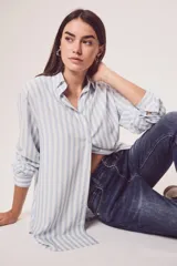 Camisa oversize celeste y blanca a rayas verticales, de mangas largas con puños abotonados y cuello camisero.