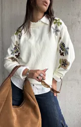 Sweater de punto color natural con cuello redondo y mangas largas, decorado con bordados florales multicolores en las mangas y hombros.