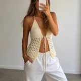 Top de crochet color crema con diseño halter, escote profundo y cierre frontal con tiras ajustables. La parte superior presenta un tejido cerrado y la parte inferior un patrón calado.