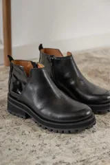 Botinetas negras con suela track, combinando cuero texturizado en la parte frontal y cuero charolado en la parte trasera. Diseño de caña baja con detalle de corte lateral.