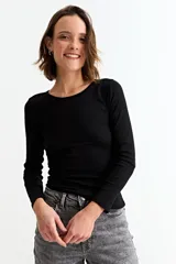 Sweater de tejido de punto fino en color negro, con cuello redondo y mangas largas. Presenta una textura acanalada y un ajuste al cuerpo.