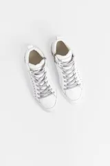 Zapatilla de caña media confeccionada en cuero vacuno blanco, con detalles de glitter plateado en los laterales y apliques de remaches metálicos. Cuenta con cierre lateral para facilitar el acceso y suela de caucho.