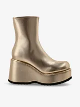 Bota corta dorada, estilo botín, con caña ajustada y punta redonda. Presenta una plataforma y taco cuña muy altos, con suela dentada negra.