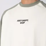 Remera de algodón con mangas raglán color verde militar y cuerpo color crudo, con cuello redondo y diseño estampado en el pecho con el texto 'ART DEPT. VCP'.