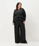 Pantalón de corte wide leg confeccionado en poliuretano con acabado liso que imita el cuero. Presenta cintura elástica con cordón de ajuste, bolsillos laterales embutidos y una silueta fluida y amplia.