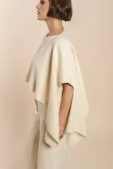 Poncho color beige con diseño a cuadros, cuello bote y terminaciones desflecadas. Tiene aberturas para los brazos en los laterales y detalles en cuero.
