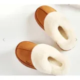 Pantuflas de gamuza negra con plataforma, forradas internamente con corderito sintético color crema. Presentan un diseño sin talón y detalle bordado en el empeine.