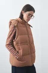 Chaleco puffer negro con diseño acolchado, capucha desmontable y cierre frontal. Cuenta con cordones ajustables en la cintura y bolsillos laterales.