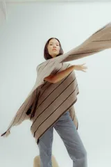 Ruana de tejido de punto con diseño a rayas horizontales en tonos beige y negro, con terminación de flecos en los bordes.