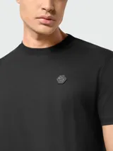 Camiseta negra de manga corta con cuello redondo y un pequeño aplique hexagonal con logo en el pecho izquierdo.