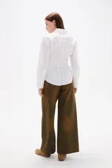 Camisa blanca de poliéster con cuello clásico, manga larga con puños anchos y detalle de frunces en la cintura que crea un efecto entallado.