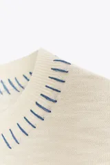 Top de punto color crudo, sin mangas, con cuello redondo y ribetes negros en las sisas. Presenta detalles de costura decorativa en azul y negro en el escote y el bajo.