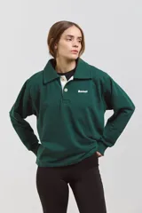 Buzo de algodón en color verde inglés, con diseño de cuello tipo chomba con botones frontales y detalles en blanco. Presenta un corte holgado y cómodo con mangas largas.